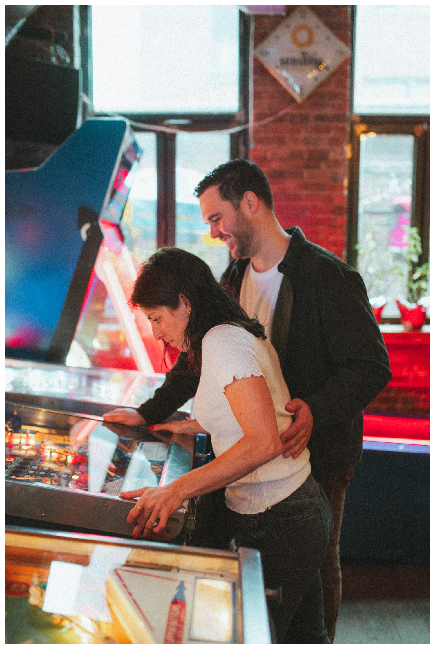 Engaged couple at Sunshine Laundromat Pinball Bar in Greenpoint Brooklyn playing pinball. Brooklyn Wedding Photographer. Parr Photo Co.