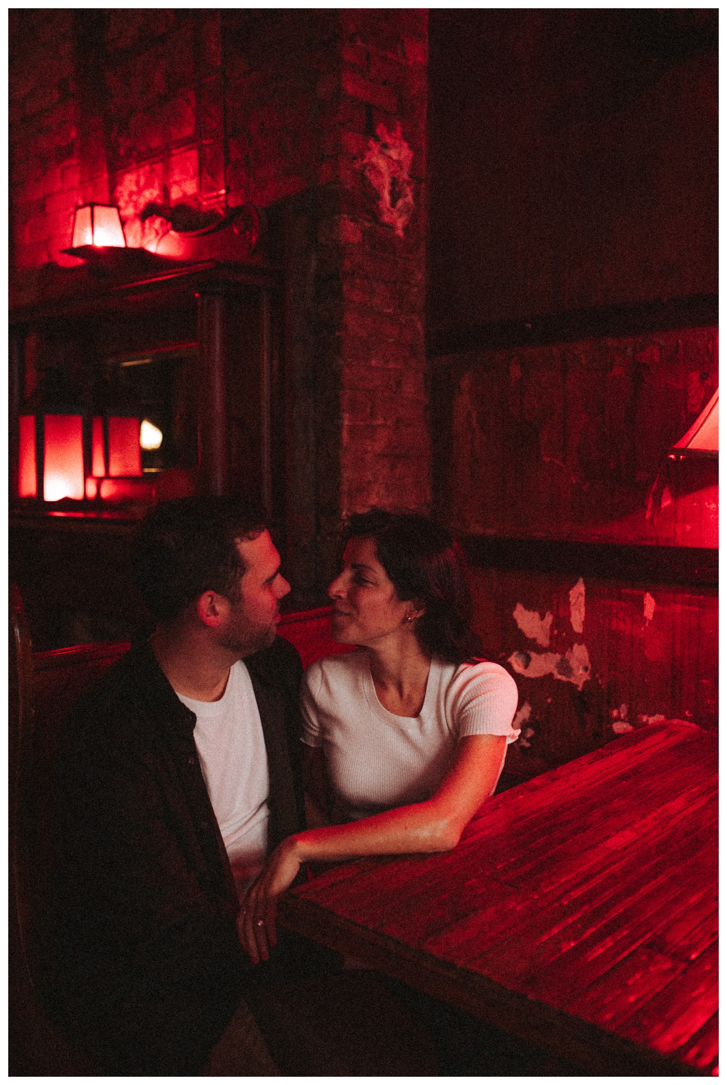 Engaged couple sitting in a bar under red light in Greenpoint Brooklyn. Brooklyn Wedding Photographer. Parr Photo Co