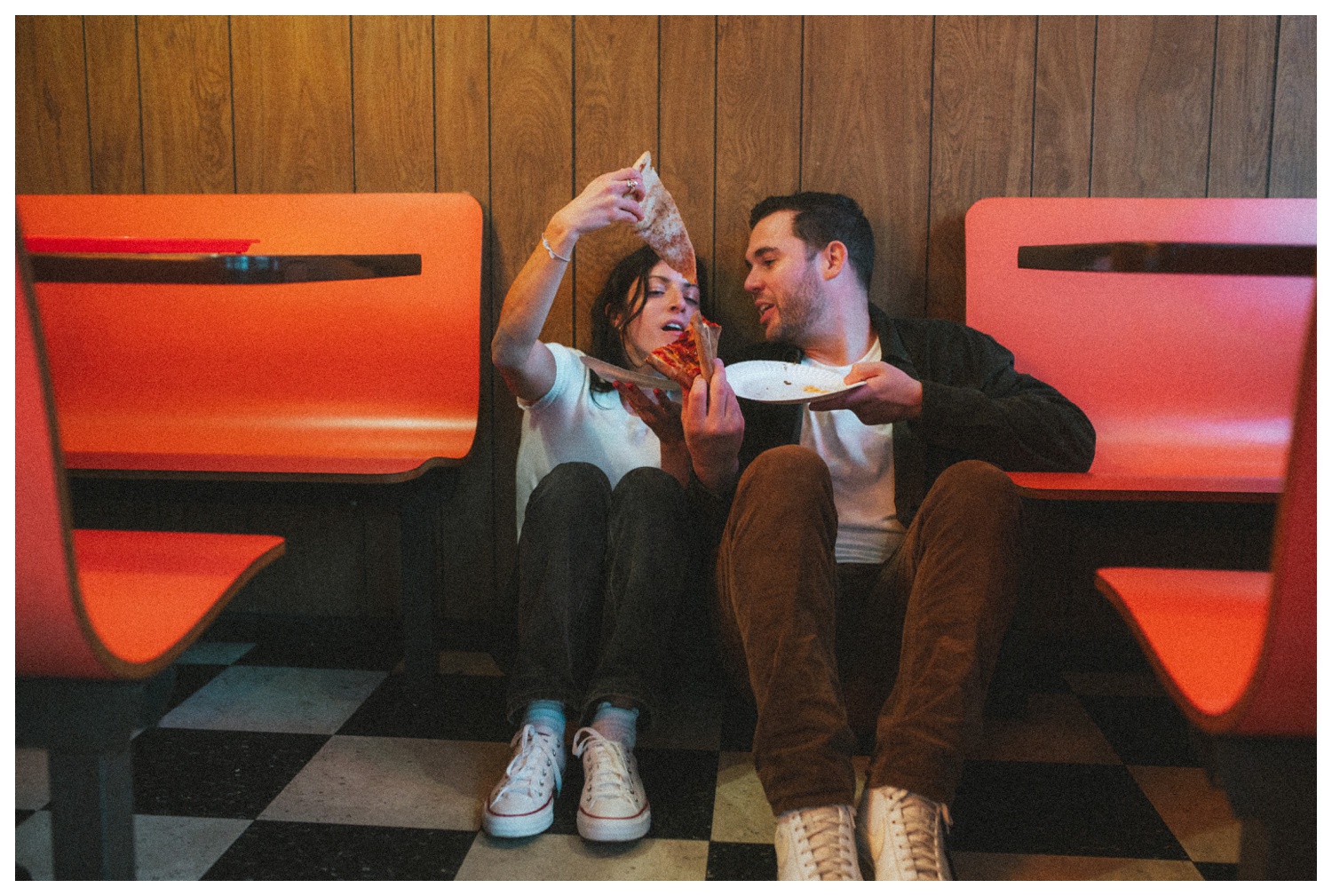 Engaged couple sitting on the floor at Paulie Gee's Slice Shop, sharing slices of pizza in Greenpoint Brooklyn. Brooklyn Wedding Photographer. Parr Photo co