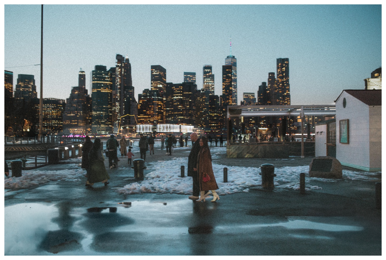 An engaged couple walking in front of the Manhattan skyline in the evening from Brooklyn. New York City wedding photographer. Brooklyn wedding photographer. Parr Photo Co.