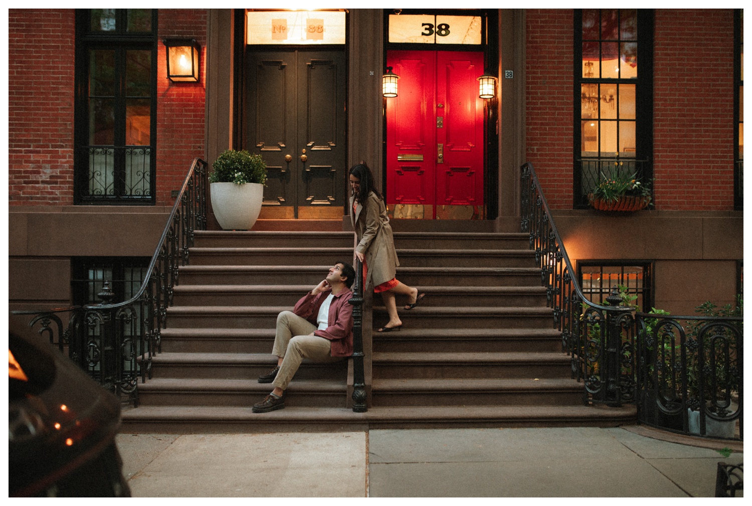 A couple sitting on teh steps of a brownstone during their engagement session in the West Village in NYC.